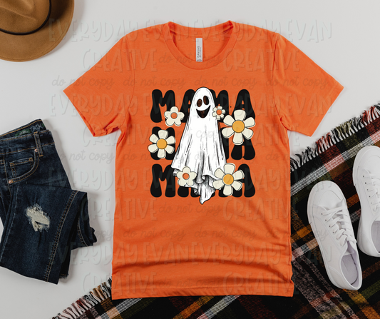Image displays a t-shirt surrounded by miscellaneous clothing items. The shirt's design includes large cute block font text that reads, "Mama mama mama" stacked together. On top of the text, a smiling sheet ghost is surrounded by white flowers varying in size and shape. 