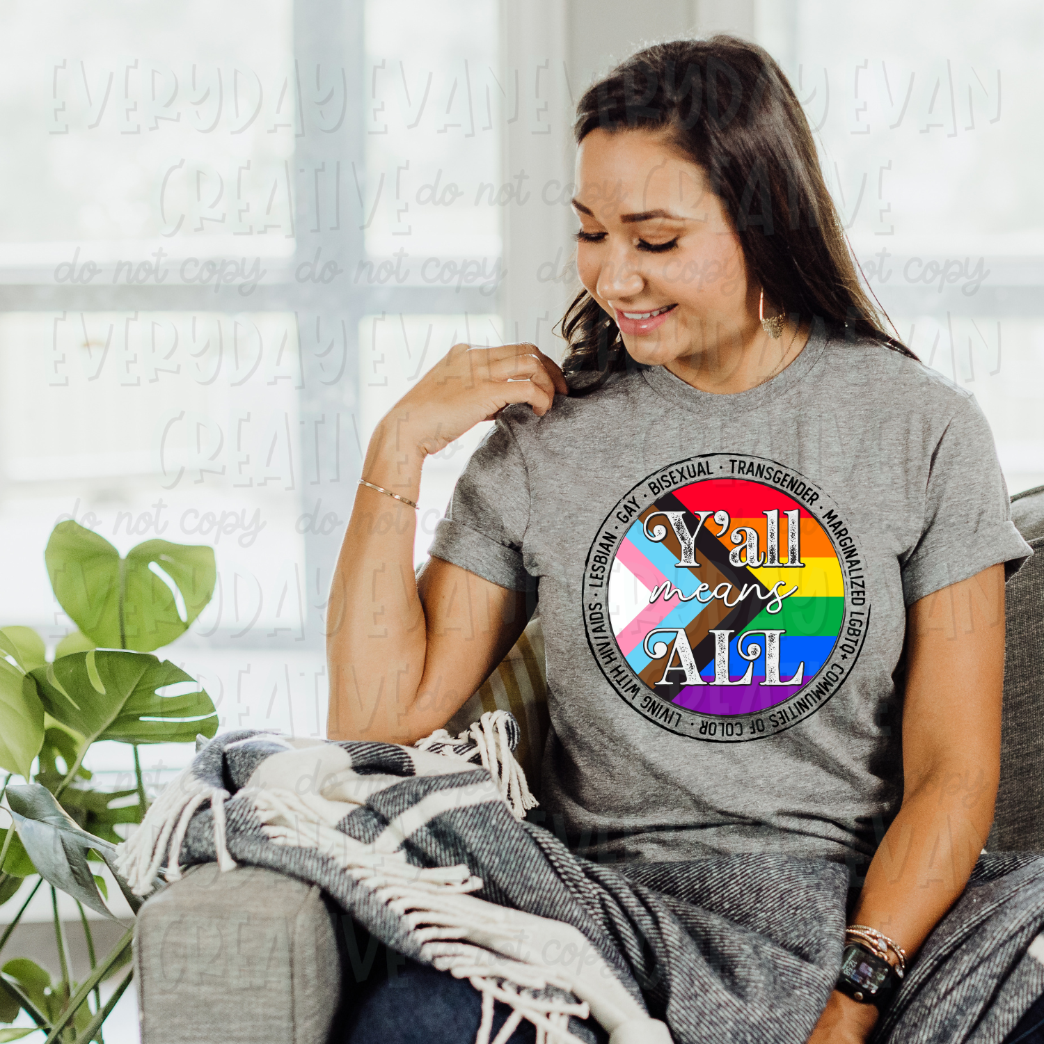 A brunette white woman sits on a couch modeling a sport gray t-shirt. The design on the shirt is a circular adaptation of the progress pride flag. In the center it says "Y'all means ALL" in white distressed lettering. Surrounding the flag are the words "Lesbian, gay, bisexual, transgender, marginalized LGBTQ+ communities of color, living with HIV/AIDS" in black all caps distressed font. There is a black distressed circle bordering these words.