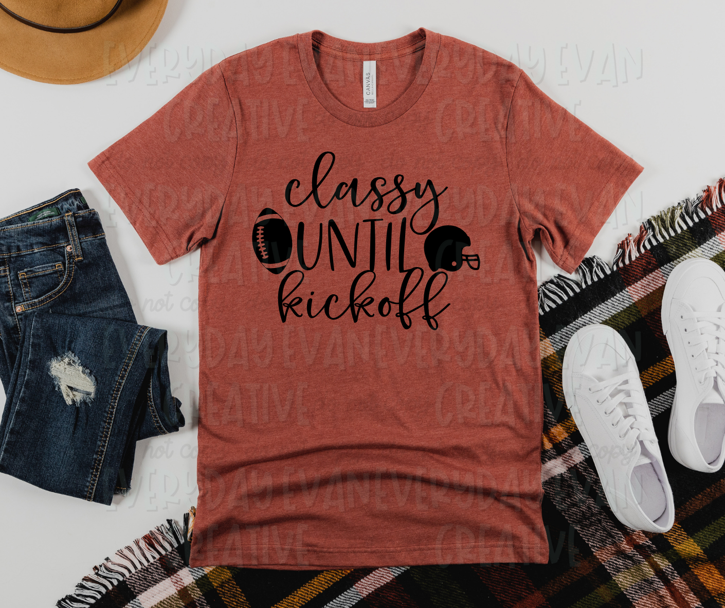 Image displays a t-shirt surrounded by miscellaneous clothing items. The shirt's design reads, "classy until kickoff" in both script and pencil font up and down the shirt with each word in its own row. Beside "until," (in the middle row) a football appears on the right and a football helmet appears on the left.