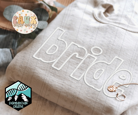 A close up image of a folded white sweatshirt. The design on the shirt says "bride" in all lowercase in a white stitch faux embroidered font. 