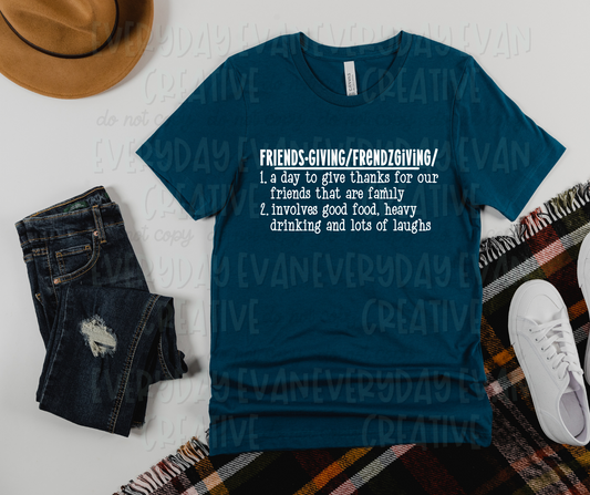 A flat lay of a t-shirt surrounded by miscellaneous clothing items. The shirt's design has a definition of friendsgiving. The text on the shirt reads, "friendsgiving/frendzgiving/1. a day to give thanks for our friends that are family. 2. involves good food, heaving drinking and lots of laughs."