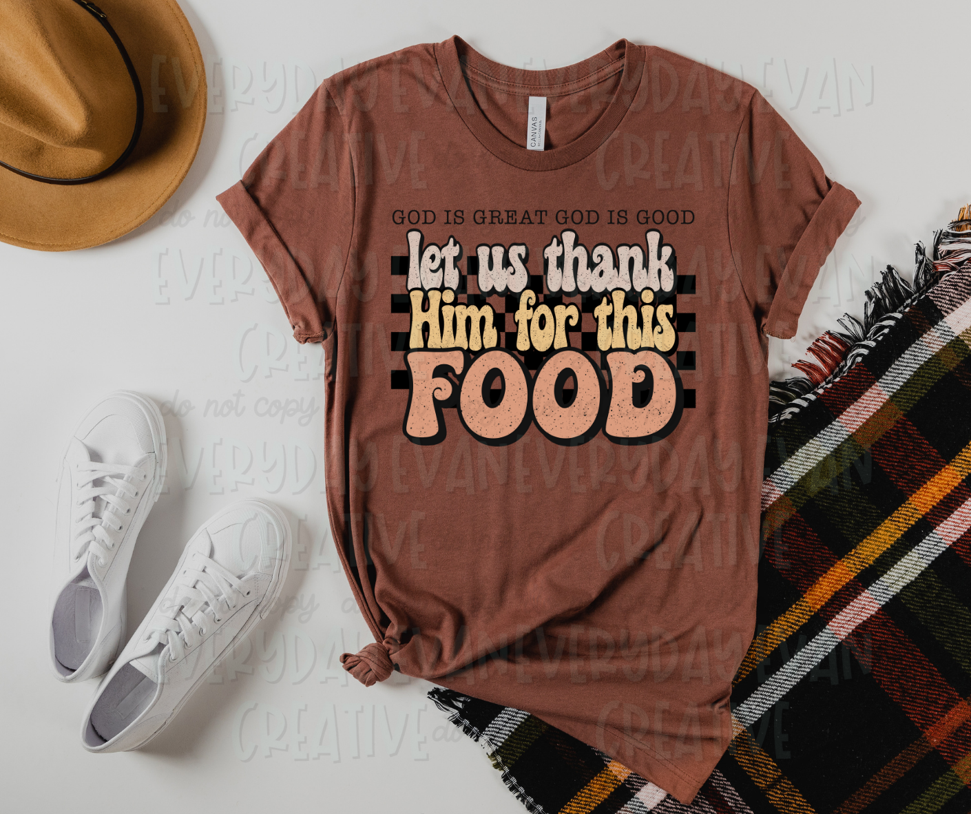 Image displays a t-shirt surrounded by miscellaneous clothing items. The shirt's design includes a checkered design behind text, in funky font of pale colors, that reads, "let us thank Him for this food." Above the design, serif font text reads, "God is great God is good."