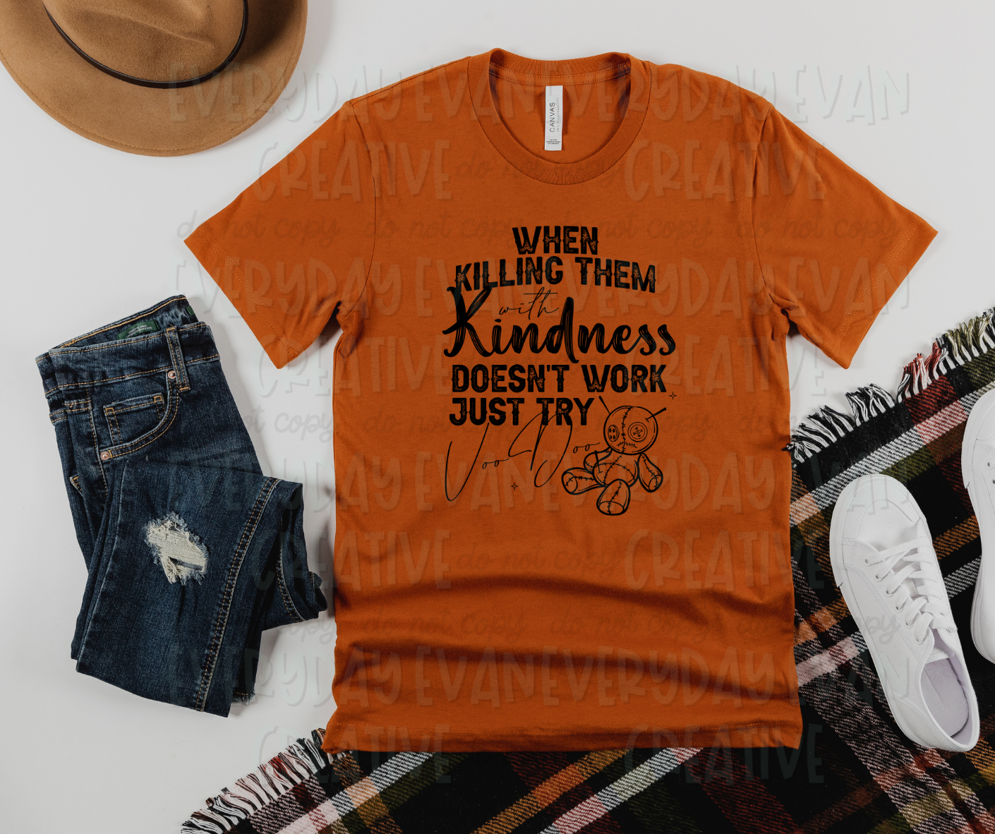 Image displays a t-shirt surrounded by miscellaneous clothing items. The shirt's design reads, "when killing them with kindness doesn't work just try voo doo" in varying fonts. On the bottom left, there is an effigy doll below the main text.
