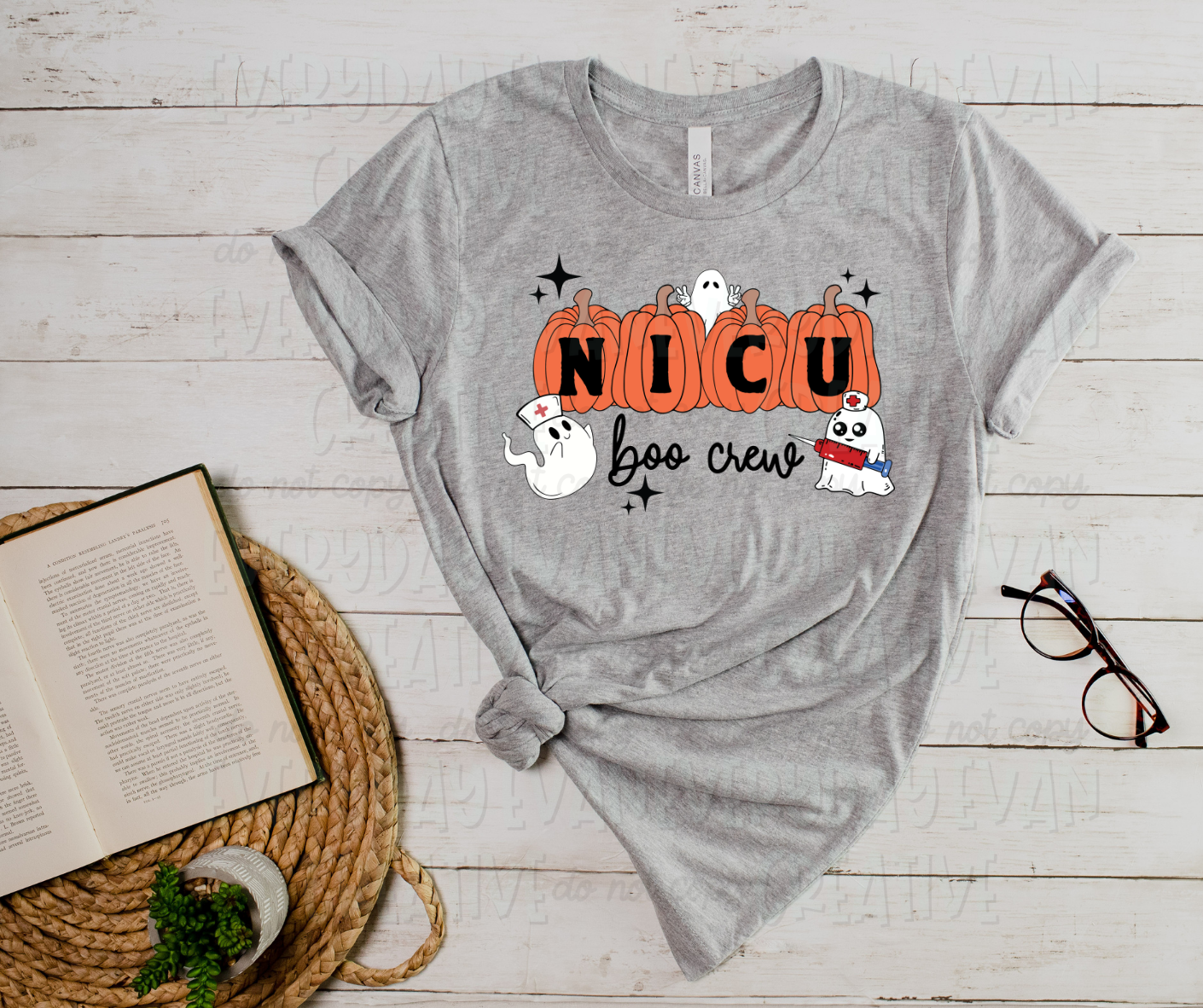 image displays a t-shirt surrounded by miscellaneous desk items. The shirt's design includes four orange pumpkins with "NICU" written in them in block text font. Below the pumpkins, in script font, it reads "boo crew." Three sheet and cartoon ghosts surround the design designed with needles and nurse caps. Starbursts surround the design.