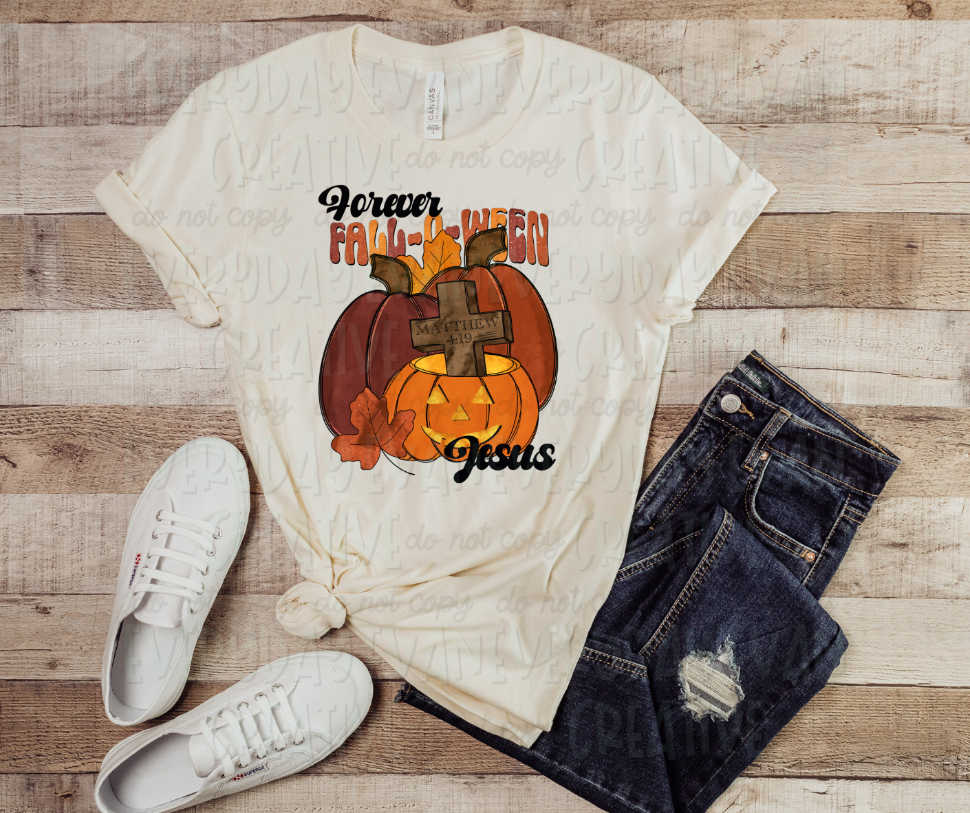 Image displays a light cream colored shirt surrounded by dark jeans and white shoes with a wood backgorund. The shirt has decorative pumpkins, one with a face carved out, and several fall colored leaves. In the carved pumpkin, a cross with "Matthews 4.19" text sticks out of the top. The pumpkins are surrounded by script text font that reads "Forever Fall-O-Ween" on top, and "Jesus" on the bottom in mixed colored text.