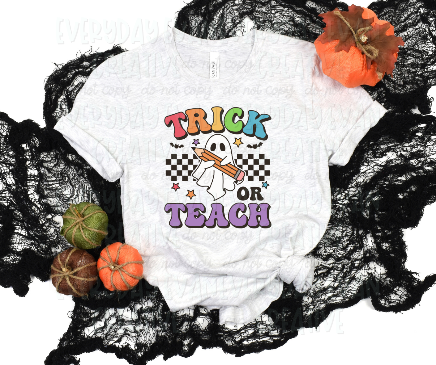 Image displays a t-shirt surrounded by fall-themed decorations. The shirt's design includes a black checkered strip behind a sheet ghost holding a pencil. Bats and rainbow-colored stars surround the design. Above the design in funky block font text, it reads "trick" in alternating rainbow colors. Below the design in the same font, it reads "or teach" in all black and purple respectively.