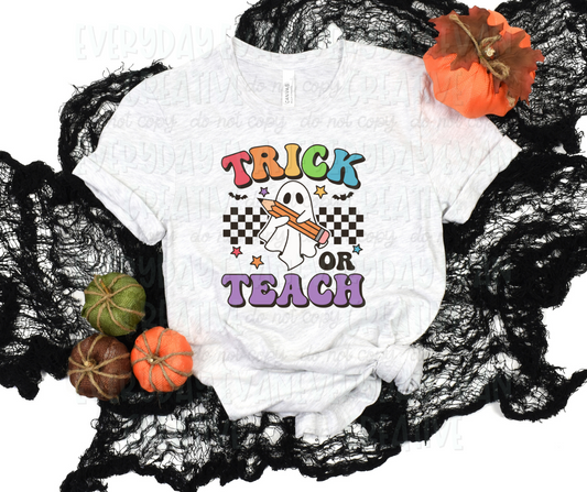 Image displays a t-shirt surrounded by fall-themed decorations. The shirt's design includes a black checkered strip behind a sheet ghost holding a pencil. Bats and rainbow-colored stars surround the design. Above the design in funky block font text, it reads "trick" in alternating rainbow colors. Below the design in the same font, it reads "or teach" in all black and purple respectively.
