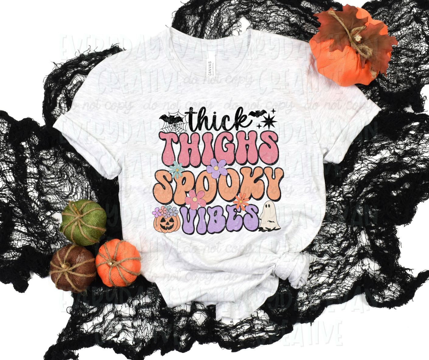Image displays a t-shirt surrounded by fall-themed decorations. The shirt's design includes text, in funky bubble font and script font, that reads, "thick thighs spooky vibes." A pumpkin, sheet ghost, starbursts, flowers of various sizes and colors, bats, and a spider web accent the design. 