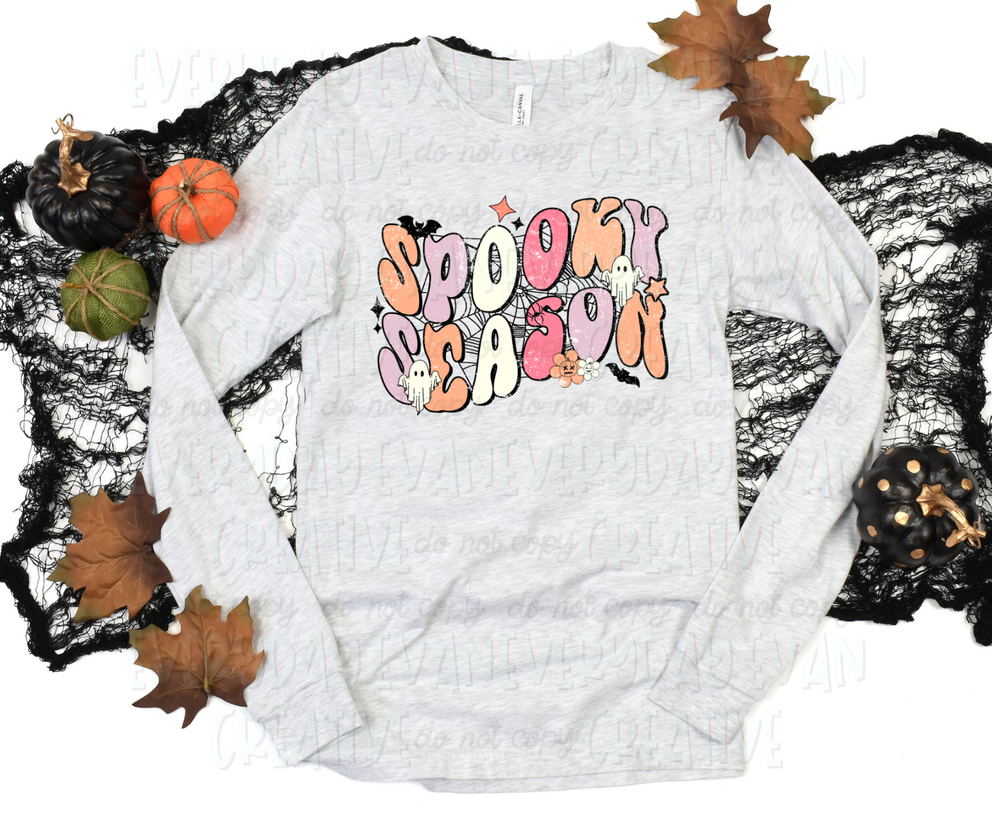 Image displays a t-shirt surrounded by fall-themed decorations. The shirt's design includes script block font text that reads "spooky season" in alternating orange, purple, white, and pink colors. The text is in front of a web design and surrounded by starbursts, bats, sheet ghosts, and accent flowers.