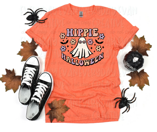 Image displays a t-shirt surrounded by fall-themed decorations. The shirt's design includes a sheet ghost with peace-sign glasses on. Text surrounding the ghost reads, in funky block font, reads, "hippie Halloween" in pale purple, orange, and pink colors. Flowers, starbursts. and bats surround the design. 