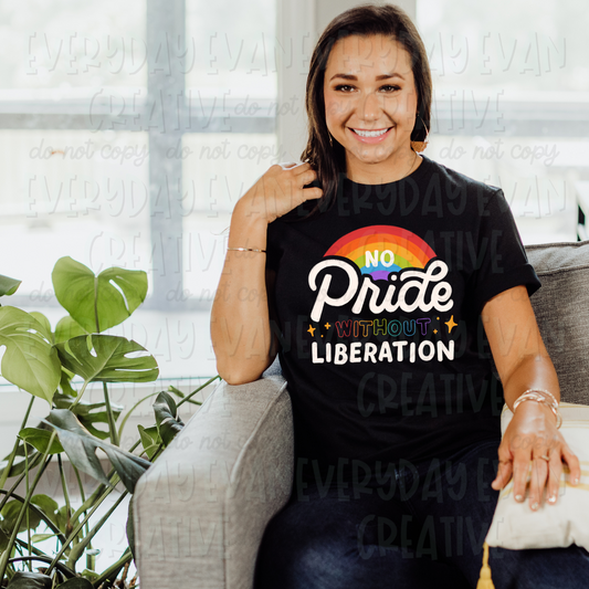 A brunette white woman sits on a couch modeling a black t-shirt. The design on the shirt begins with a rainbow. In the center of the rainbow it says "no" in white block letters. Directly underneath the rainbow is the word "pride" in large white script font. Underneath is the word "without" in rainbow hollow outline front with starbursts on either side. The bottom of the design says "liberation" in block white lettering. 